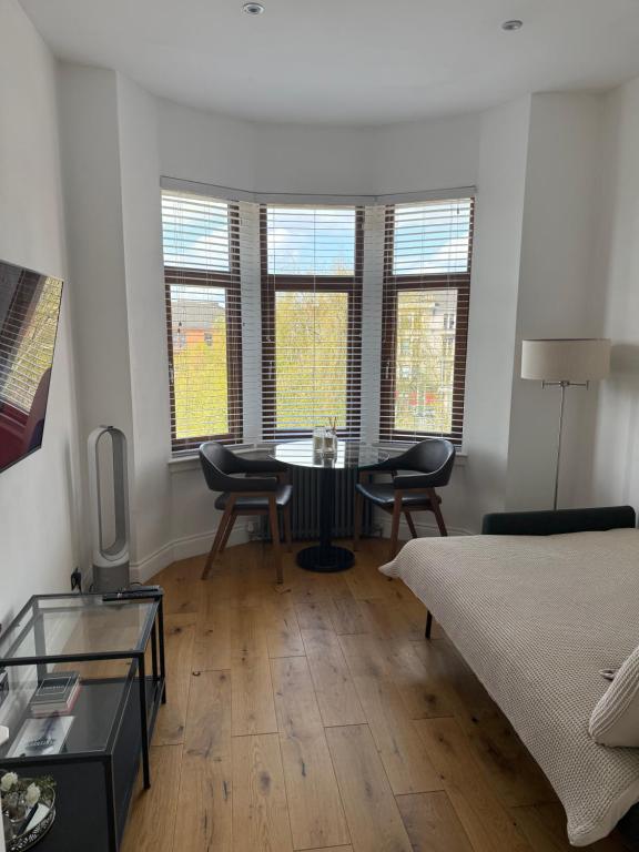 a room with a bed and a table and windows at Top Floor West End Flat - 3-Min Walk to Subway - Park Views in Glasgow