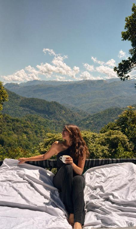 a woman sitting on a bed with a cup of coffee at Scenic Mountain Cabin with Workspace - Close to Ella in Badulla