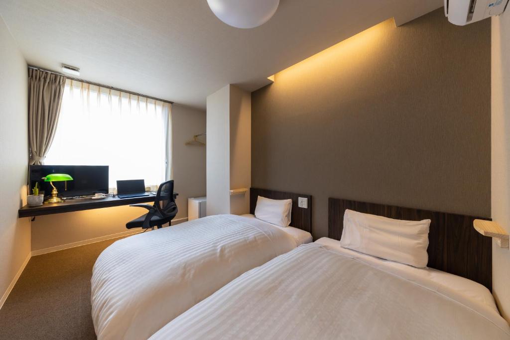 a bedroom with two beds and a desk and a window at Business Hotel Hayashiso in Miyazaki