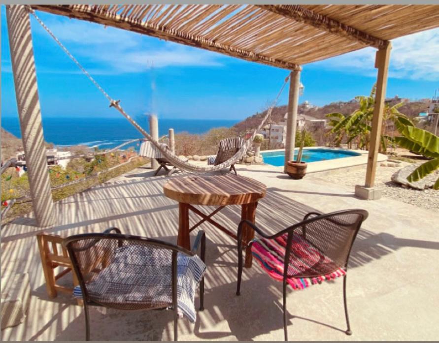 a porch with two chairs and a table and a hammock at Macondo GuestHouse Beach in Playa Estacahuite