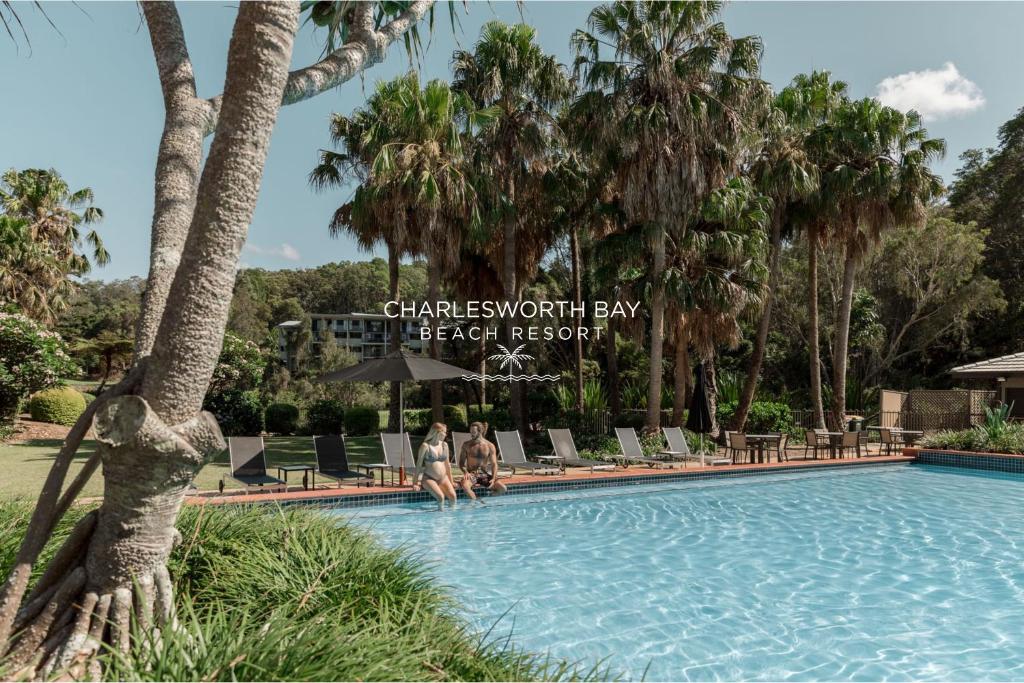a swimming pool with palm trees and a sign at Charlesworth Bay Beach Resort in Coffs Harbour