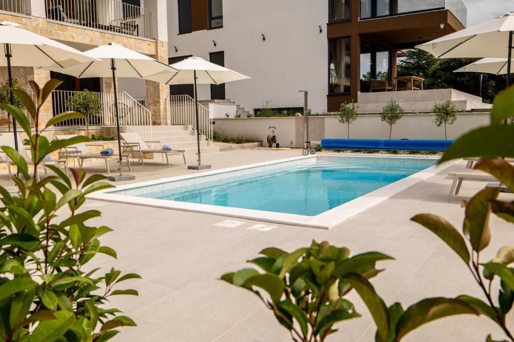 a swimming pool with umbrellas next to a building at Kožino Bay Lodge - Brand New Seaside Apartments, Heated Pool in Kožino