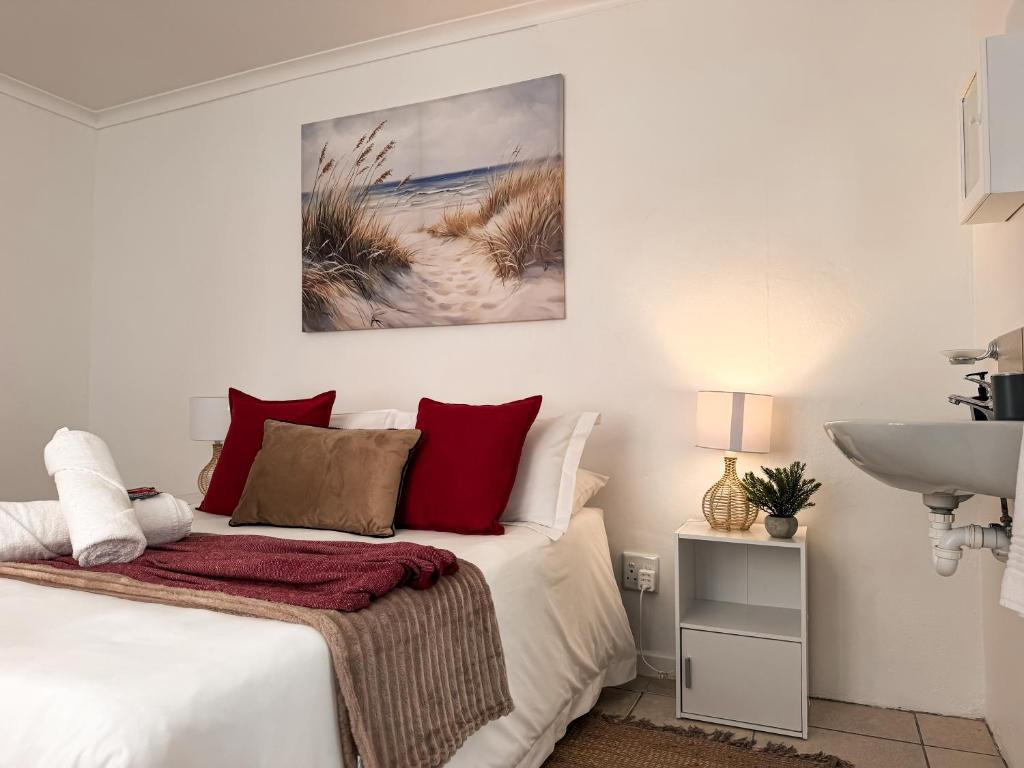 a bedroom with a bed with red pillows and a sink at Paterson Place Studios in Hermanus