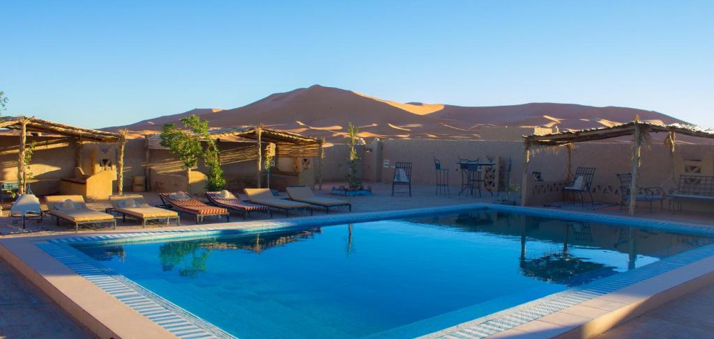 een groot zwembad met stoelen en een berg op de achtergrond bij Auberge Sahara Garden in Lac Yasmins