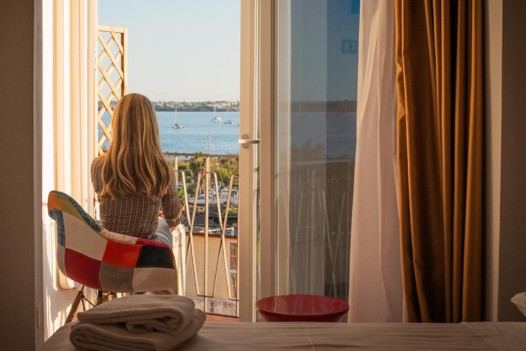 a woman sitting in a chair looking out a window at the ocean at Hotel Centrale in Syracuse