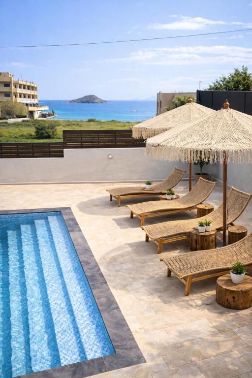 a pool with lounge chairs and umbrellas next to the ocean at Interni Villa by A&D Properties in Porto Rafti
