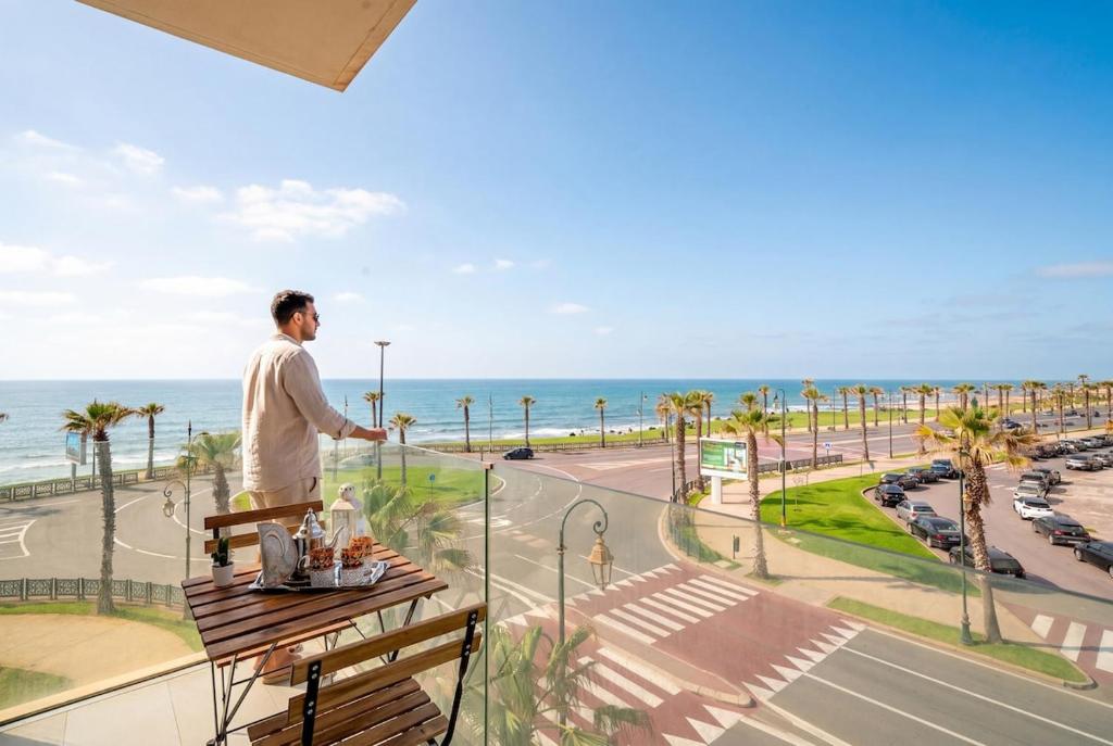 a man standing on a balcony looking out at the ocean at Atlantic Blue 3BR Ocean View, Rabat Corniche in Rabat