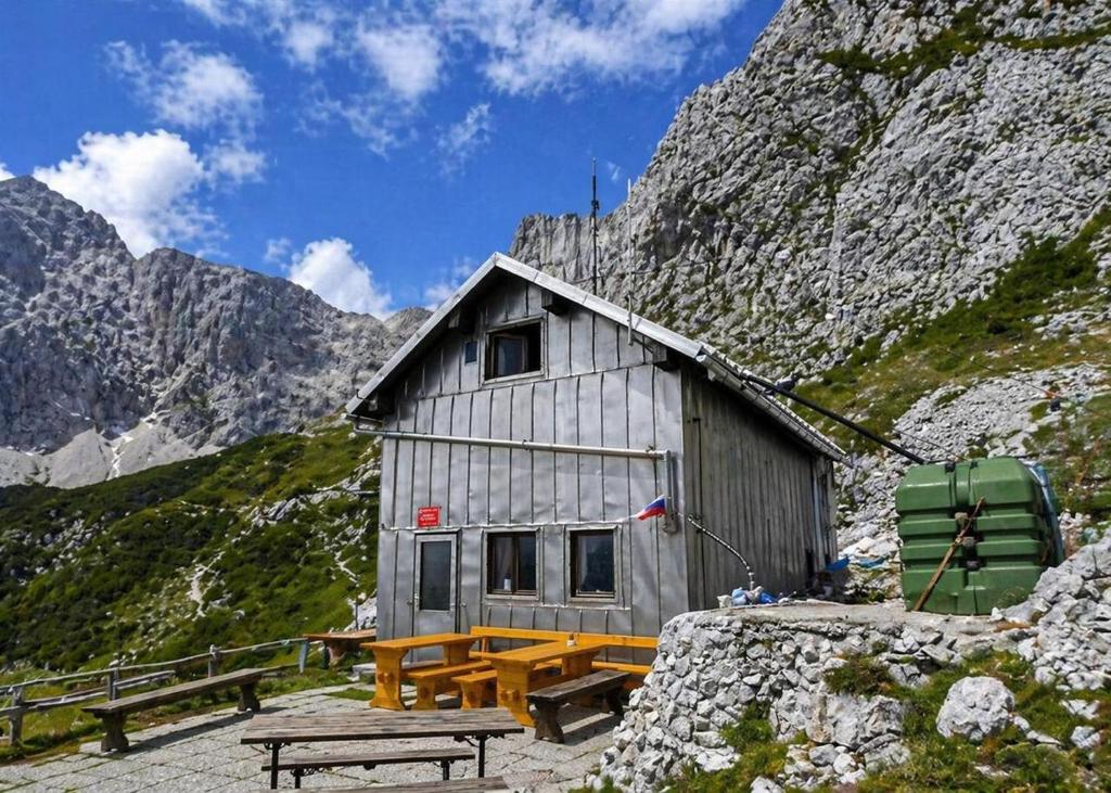 a building with a picnic table in front of a mountain at Zavetišče pod Špičko in Soča