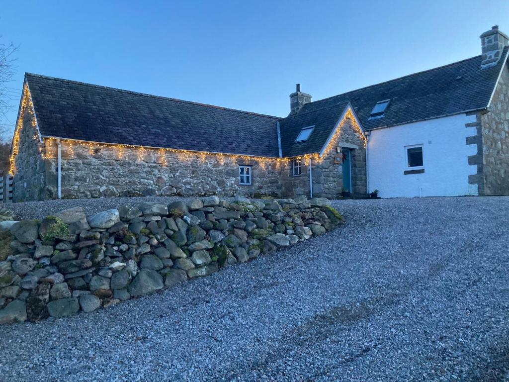 a stone building with a stone wall next to a building with lights at Jakels Rest in Lairg