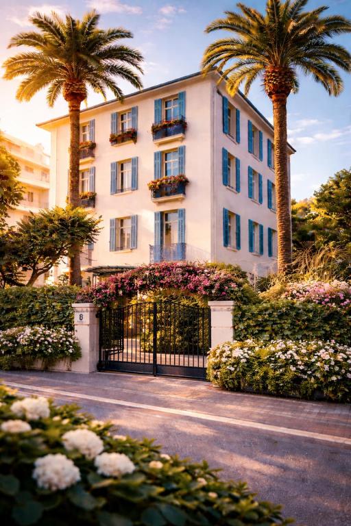 a white building with palm trees and a gate at Hôtel de charme CECIL in Juan-les-Pins