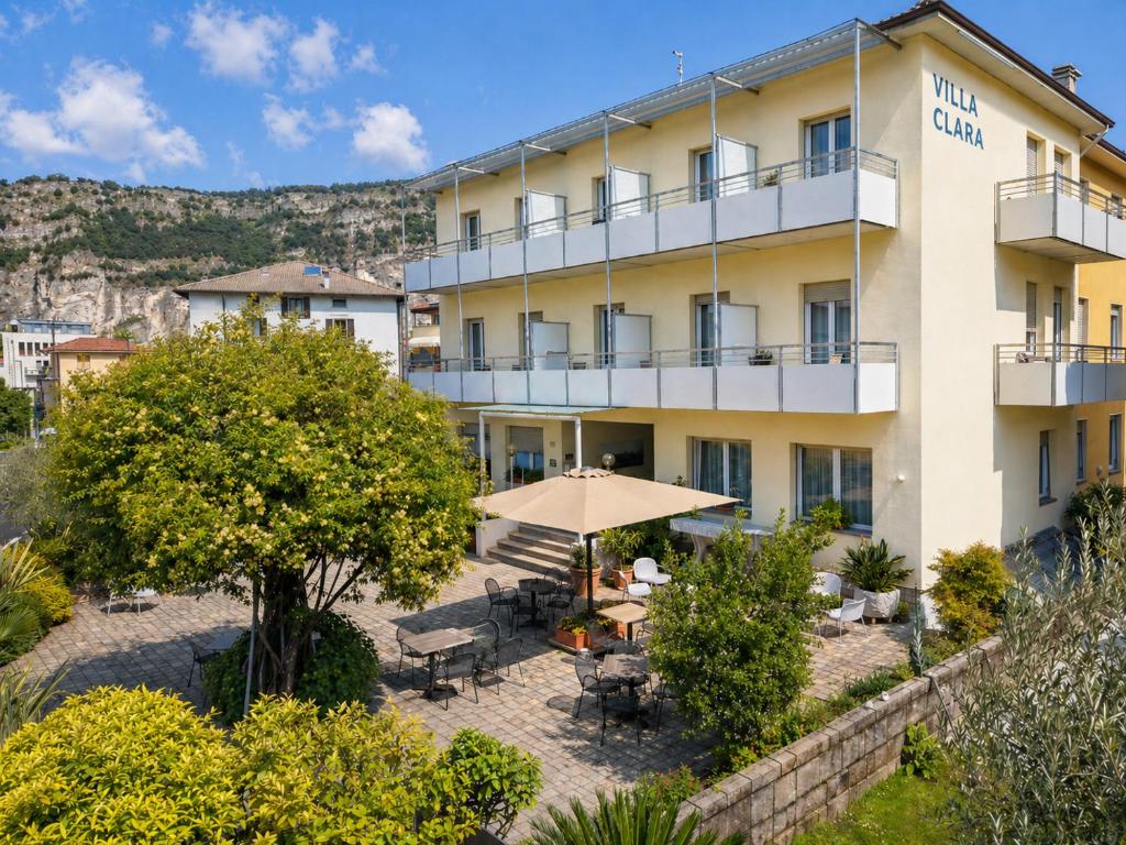 a hotel with tables and umbrellas in front of it at Hotel Villa Clara in Nago-Torbole