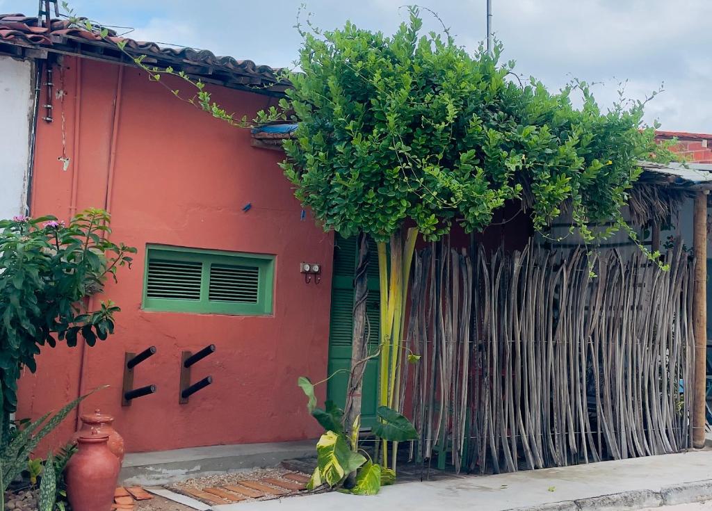 a red house with a tree next to a fence at Chalé dos Ventos Preá - CE in Cruz