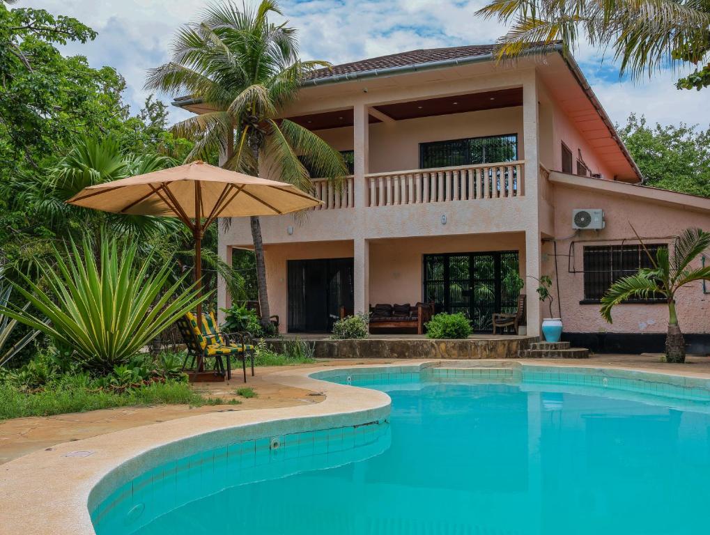 a house with a swimming pool and an umbrella at Tradewinds Lodge in Diani Beach