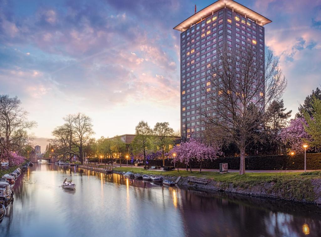 ein hohes Gebäude neben einem Fluss mit einem Boot in der Unterkunft Hotel Okura Amsterdam – The Leading Hotels of the World in Amsterdam