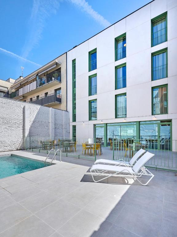 a building with a pool and a lounge chair at Hostelfly Fira Barcelona in Hospitalet de Llobregat