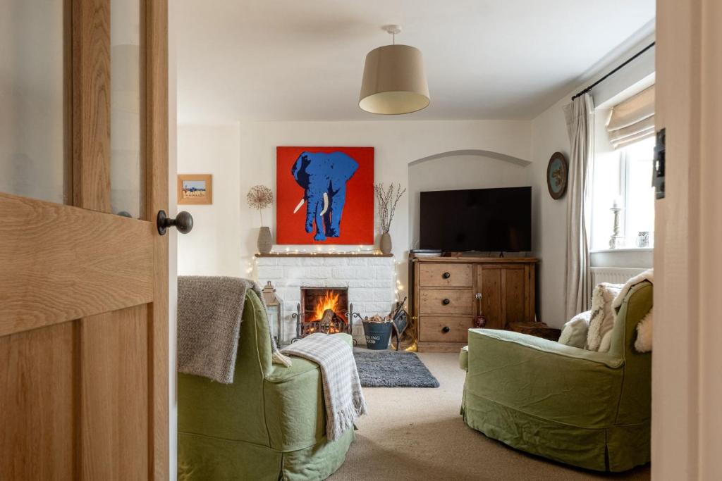 a living room with two green chairs and a fireplace at Mulberries in Adlestrop