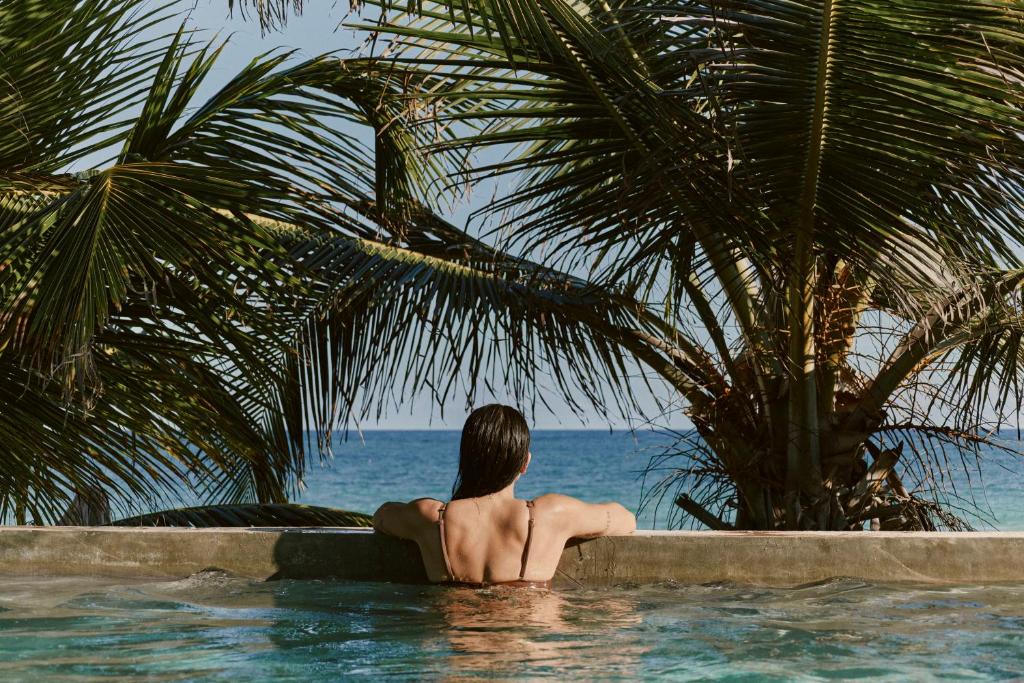 a woman sitting in a swimming pool looking at the ocean at Playa Esperanza Tulum in Tulum