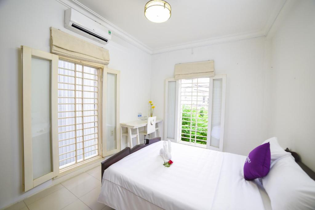 a white bedroom with a bed and two windows at Maison Vy Homestay in Hue