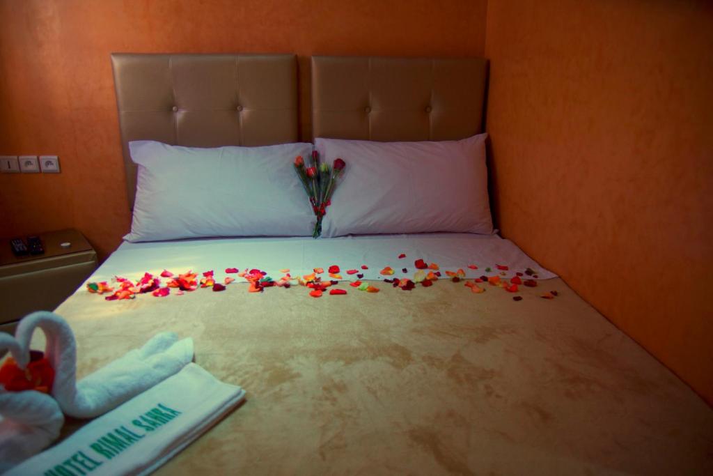 Una cama con un ramo de flores. en Hotel Rimal Sahara en El Aaiún