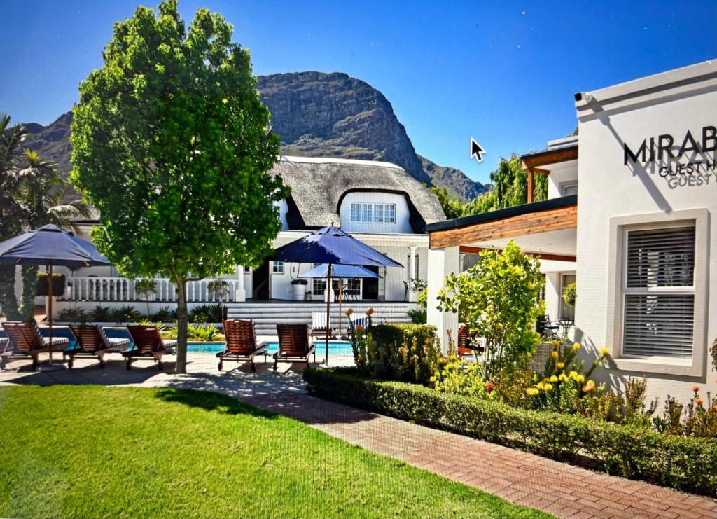 a house with a yard with chairs and umbrellas at Mirabelle Guesthouse in Franschhoek