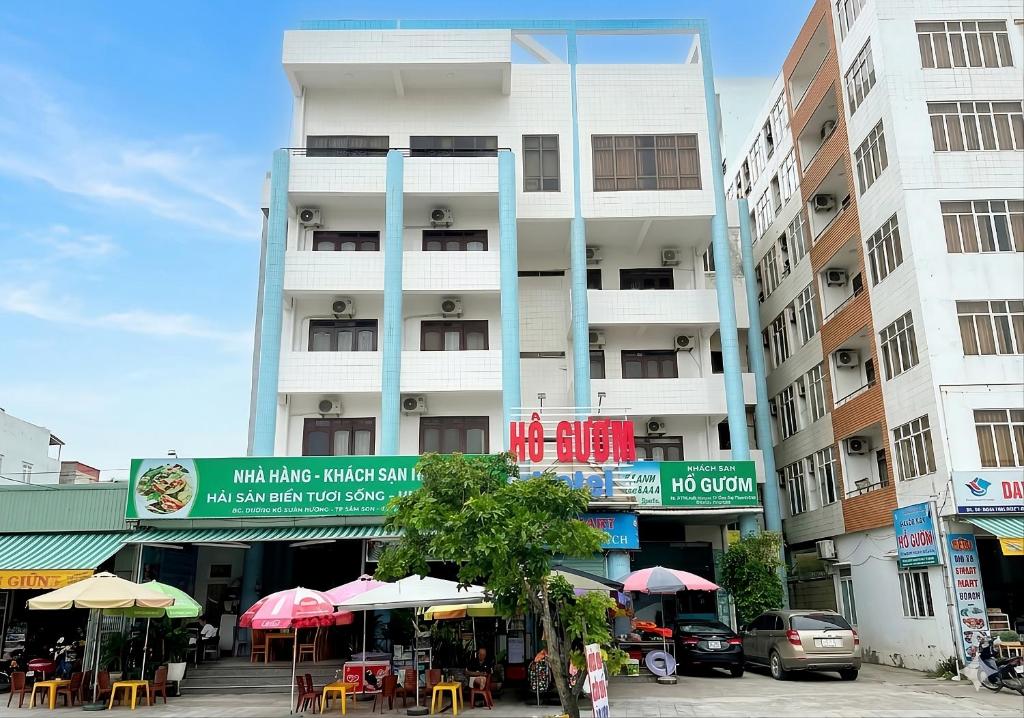 a tall building with tables and umbrellas in front of it at Khách sạn Hồ Gươm in Sầm Sơn