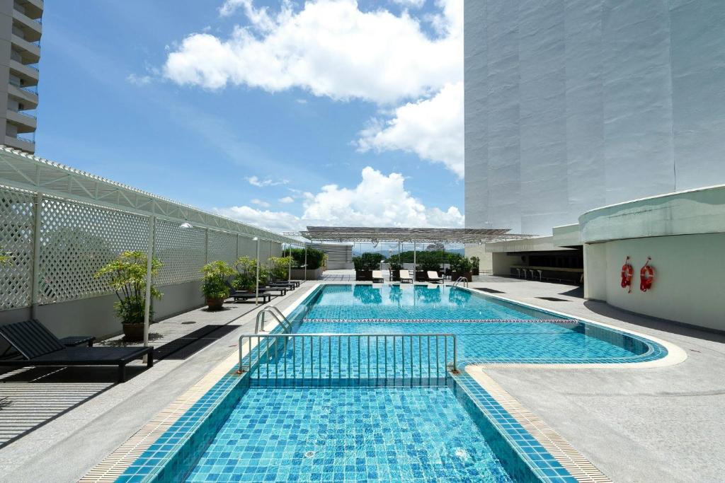 A sunny outdoor pool deck with a long tiled pool and loungers beside the building.