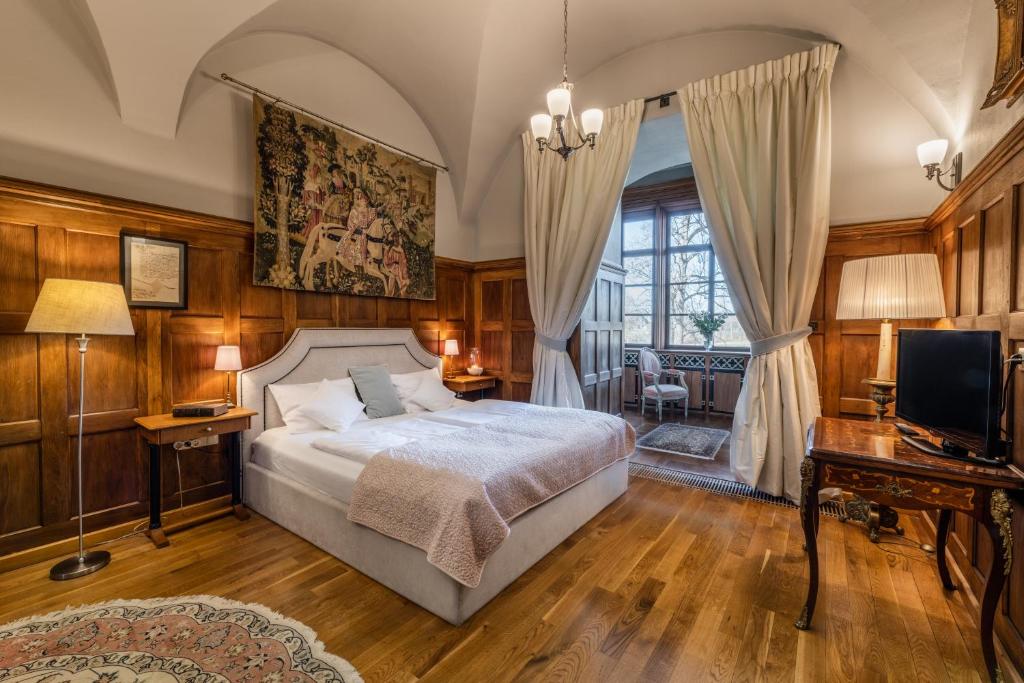 Warm wood-paneled bedroom with upholstered bed, tapestry above headboard, window alcove and soft lighting