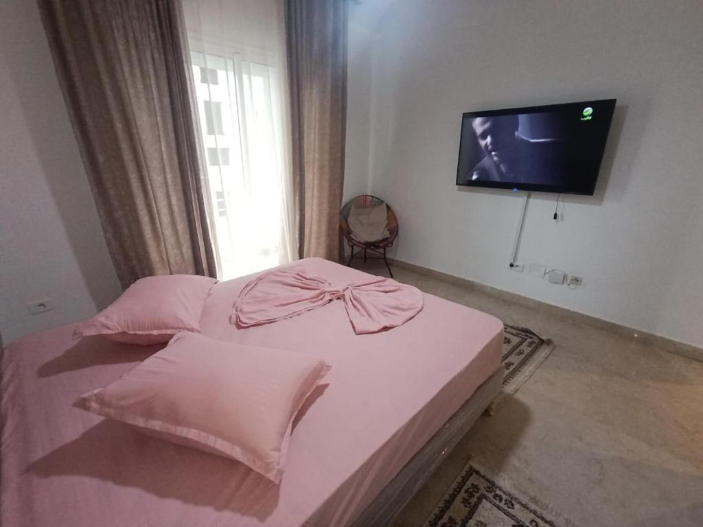 a bedroom with a bed with pink sheets and a flat screen tv at Salem in Sidi Daoud