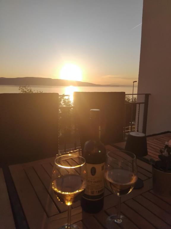 a bottle of wine and two glasses on a table with the sunset at Apartmani Silvana&Vera in Senj