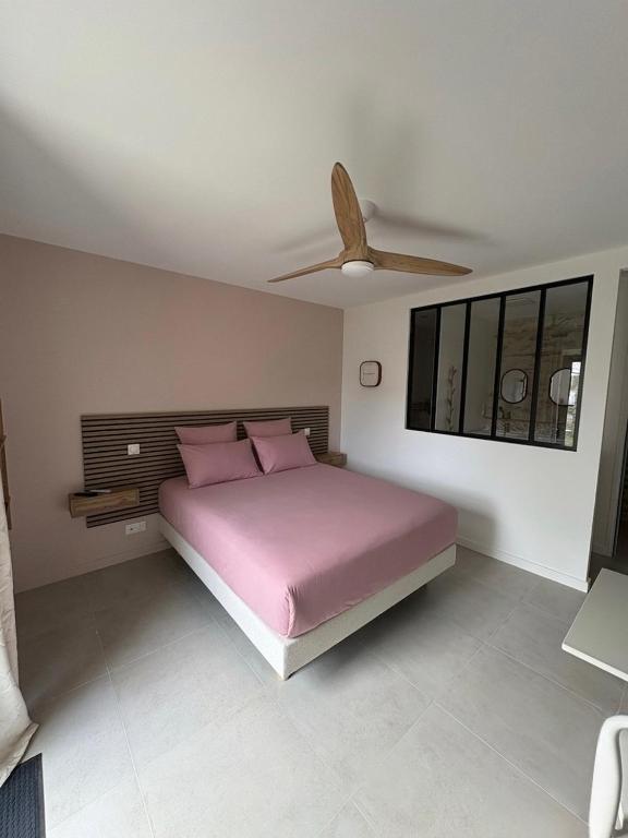a bedroom with a pink bed and a ceiling fan at Chambre d'hôtes Camélia in Saint-Lyphard