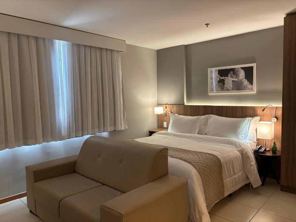 a bedroom with a bed and a chair and a window at Promenade Soho Campos dos Goytacazes in Campos dos Goytacazes