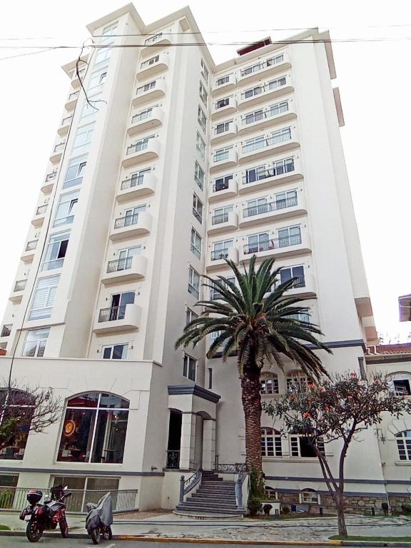 a large white building with a palm tree in front of it at TORREMIA apartamentos de lujo in Cochabamba