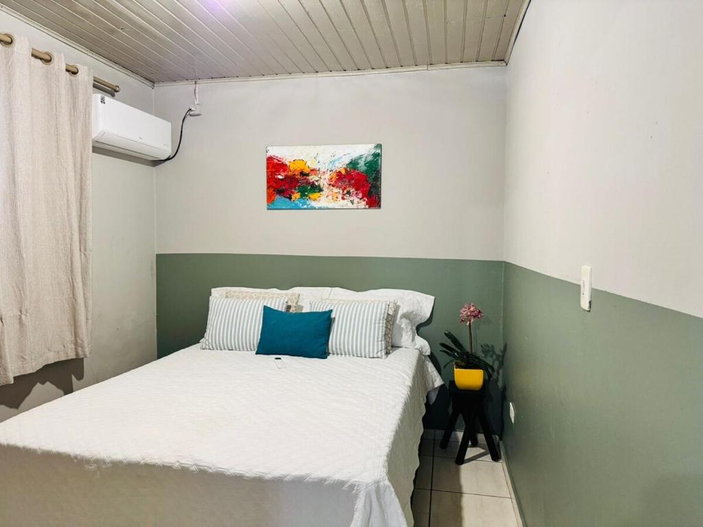 a bedroom with a bed with white sheets and blue pillows at Casa Aconchego 2, Self Check-in in Presidente Prudente