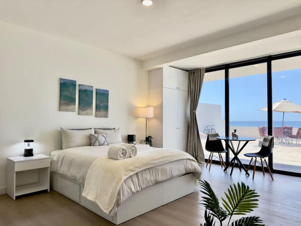 a white bedroom with a large bed and a table at Little Pearl Sea View Studio in San Antonio del Mar