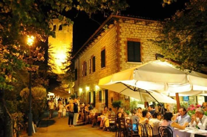grupa ludzi siedzących przy stołach przed budynkiem w obiekcie Osteria Belvedere w mieście San Leo