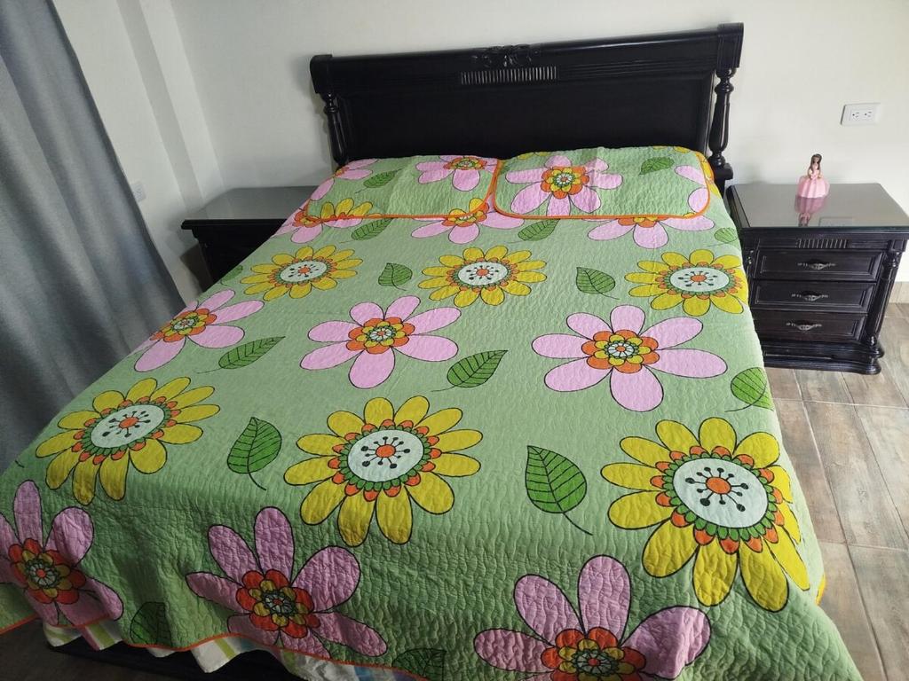 a bed with a green comforter with flowers on it at Maxi&Mia Cabañas in Coveñitas