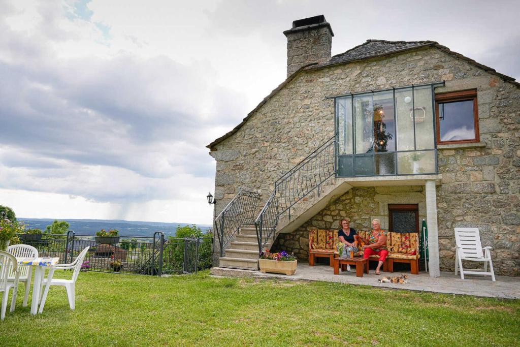 two people sitting on a bench outside of a stone house at Gîte le marlet in Saint-Alban-sur-Limagnole