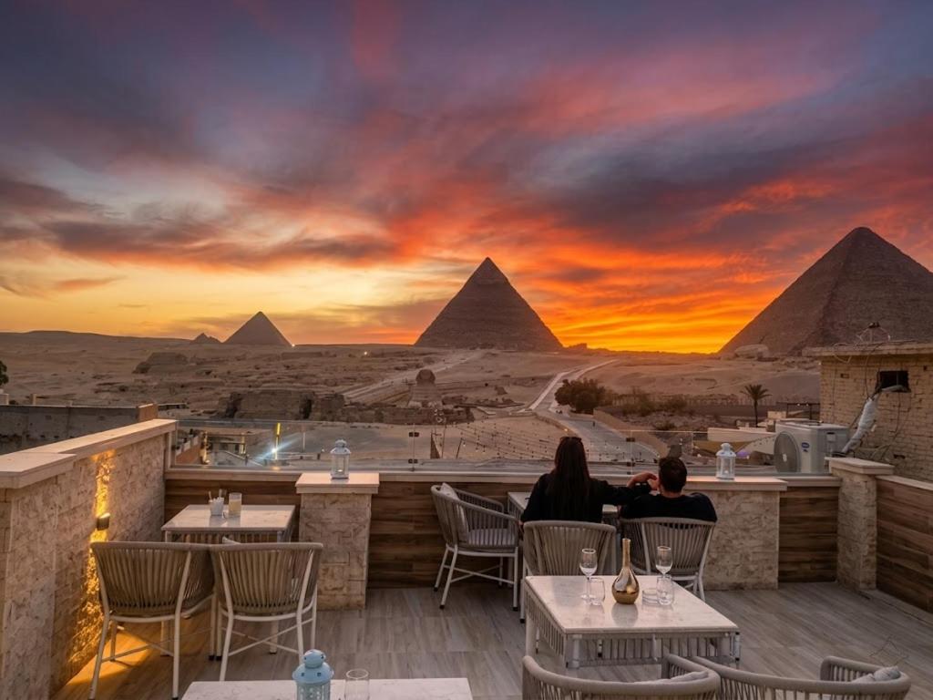two people sitting at a restaurant with the pyramids in the background at Rehana Pyramids View in Cairo