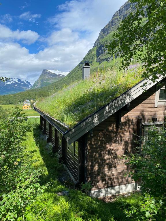 a building with a grass roof with mountains in the background at Cozy log cabin in Geiranger in Geiranger