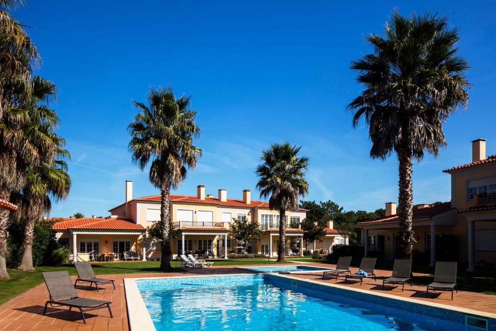 une villa avec piscine et palmiers dans l'établissement The Village – Praia D’El Rey Golf & Beach Resort, à Casal da Lagoa Seca