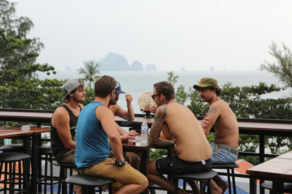 un grupo de hombres sentados en una mesa frente al océano en Balcony Party Hostel - Adult Only +18, en Ao Nang Beach