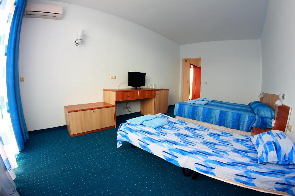 a room with two beds and a desk with a television at Hotel Akre in Kavarna