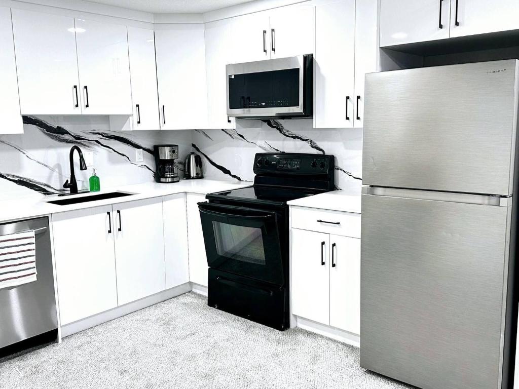 a kitchen with white cabinets and a black stove and refrigerator at Private, Cozy, Luxury, Spacious One Bedroom Suite in Airdrie