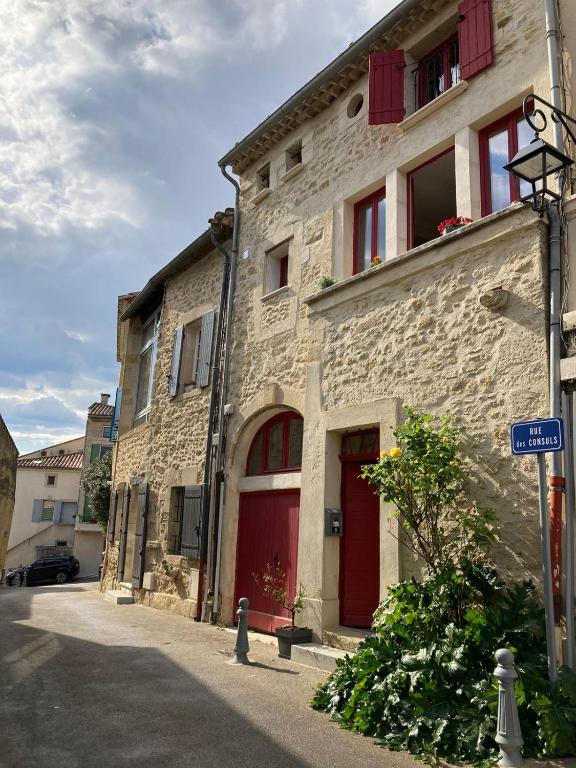 a stone building with red doors on a street at Petit cocon à 10min d'Avignon in Pujaut