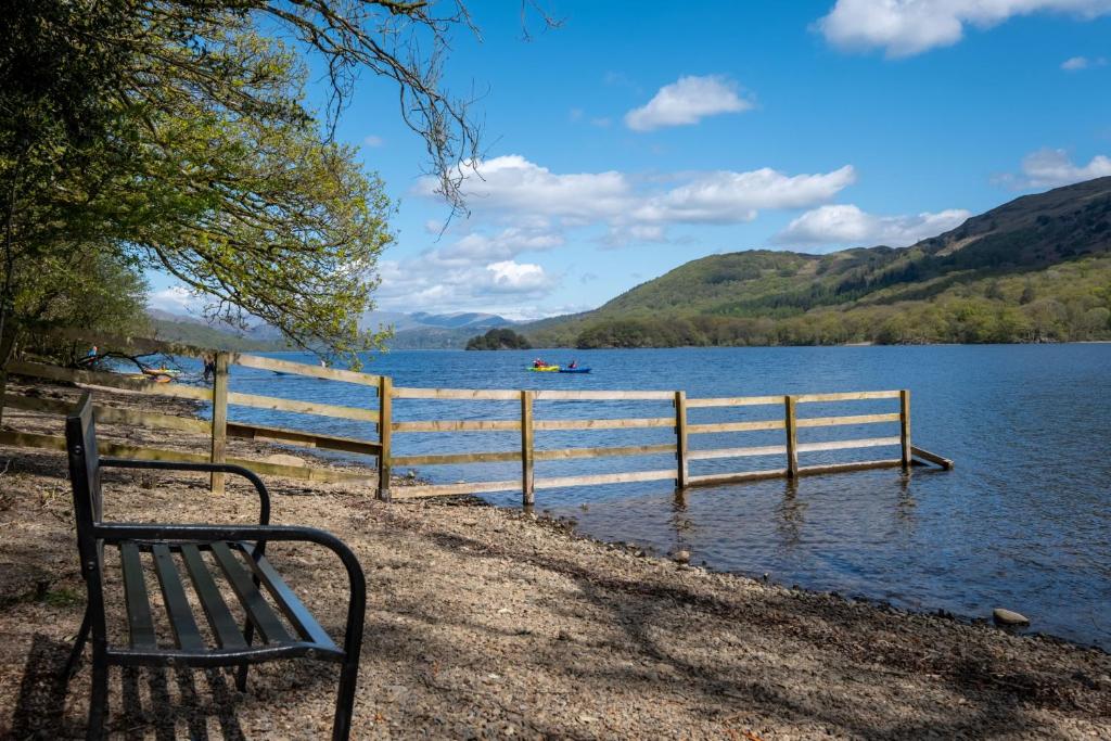 a bench sitting next to a fence next to a lake at Potter's Wheel, by the lake in High Nibthwaite