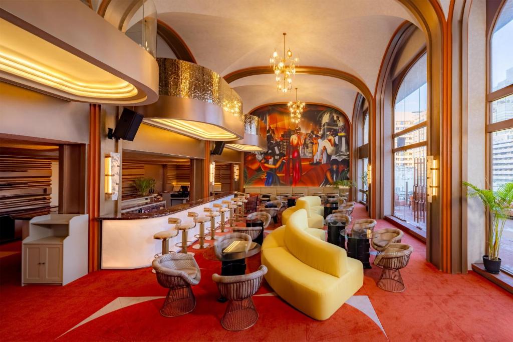 Lobby with curved bar, sculptural yellow sofa, red rug, mural and floor-to-ceiling windows with city views at Aiden Surawong Bangkok in Bang Rak