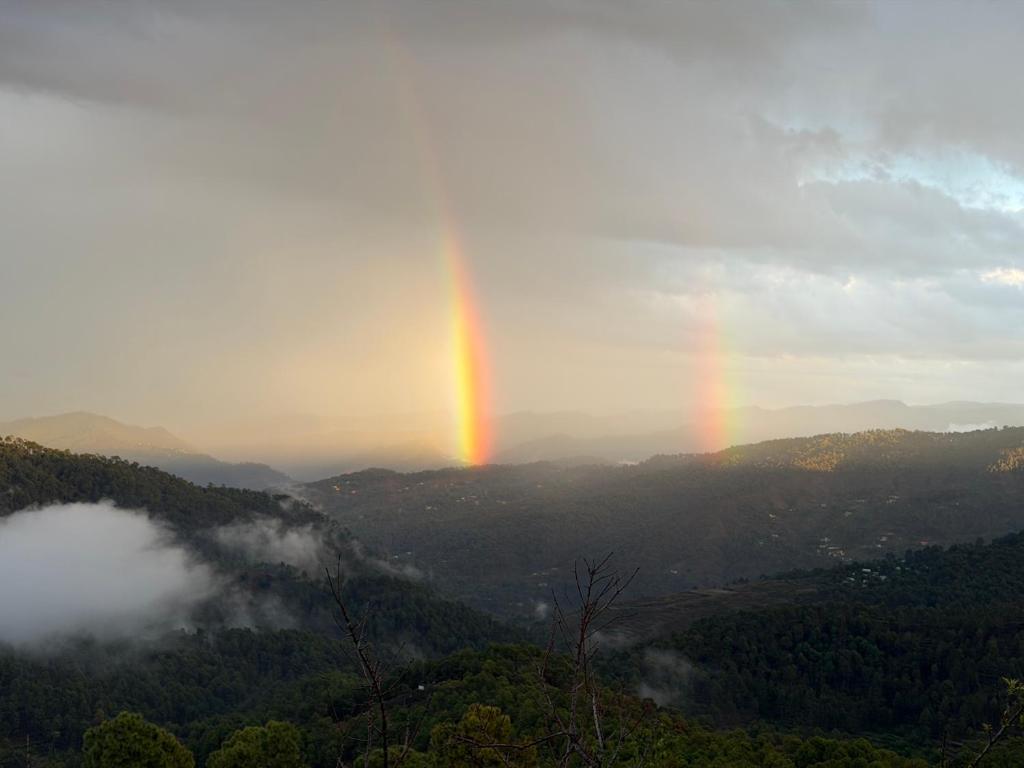 a rainbow in the sky over a valley at Terra Himalayan Homestay in Kasar Devi in Hawālbāgh