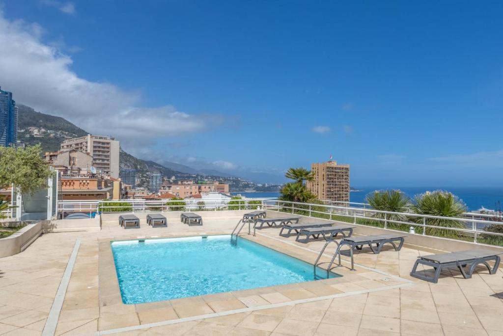 a swimming pool with benches and a view of the ocean at Le Studio des Deux Frontières in Beausoleil