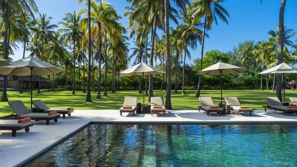 a pool with chairs and umbrellas and palm trees at Luxury Beachfront Villa in North Lombok in Gili Islands