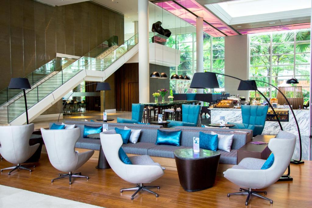 A bright lobby lounge offers clustered armchairs, sofas and tables beside an escalator.
